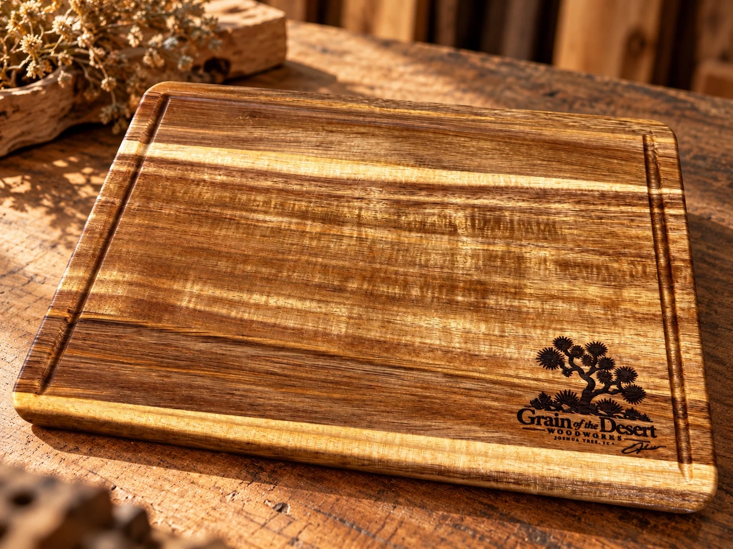 Handmade golden wood cutting board with engraved Joshua tree logo on a rustic workbench